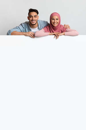 Free Place For Ad. Happy Muslim Couple Leaning At White Advertisement Boardの写真素材