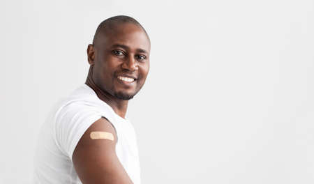 vaccination. Smiling african american man showing his arm with an adhesive bandage, copy spaceの写真素材