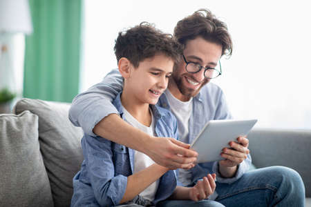 Weekend family leisure. Happy father and son using tablet computer, browsing internet online at homeの写真素材