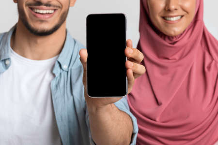 Check This App. Smiling Muslim Couple Demonstrating Smartphone With Black Blank Screenの写真素材