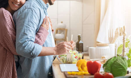 Unrecognizable Man Cooking Salad In Kitchen, Wife Embracing Him From The Backの写真素材
