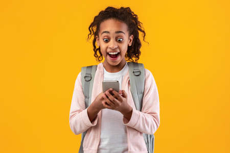 Excited surprised African American girl using mobile phone