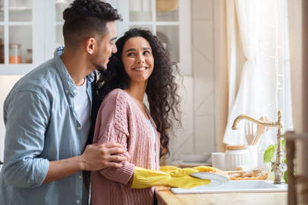 Loving Arab Husband Embracing Wife From The Back While She Washing Dishesの写真素材