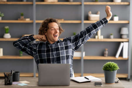 Guy At Laptop Stretching Arms And Yawning At Workplace Indoor