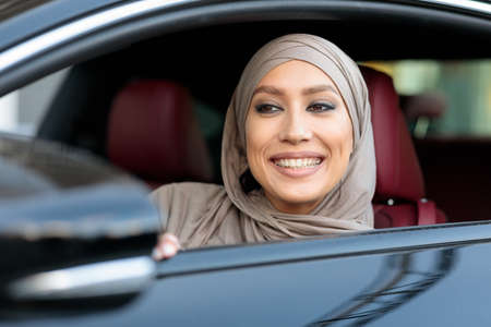 Smiling muslim woman test driving car in urban city