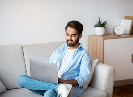 Eastern Millennial Male Using Laptop While Relaxing On Couch At Homeの写真素材