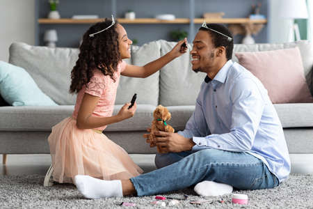 Excited little black girl putting make up on her father faceの写真素材