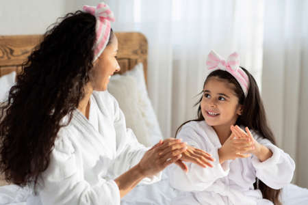 Beautiful mother and daughter applying cream on hands