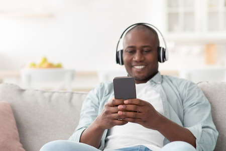 Enjoy the music. Happy black man listening audio on mobile phone with headphones, surfing internet