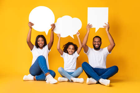 Smiling black family hoding speech bubbles at studioの写真素材