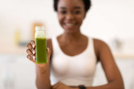 Slim African Female Showing Green Smoothie Bottle Sitting In Kitchenの写真素材