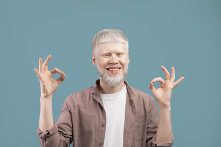 Happy blond man with unusual albino appearance meditating, keeping his fingers in mudra, blue backgroundの写真素材