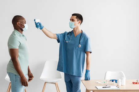 Measuring fever with gun, scanning forehead of african american man in clinicの写真素材