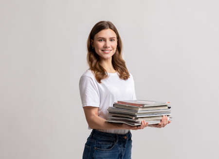 Portrait Of Smiling Millennial Female With Stack Of Paper Magazines In Handsの写真素材