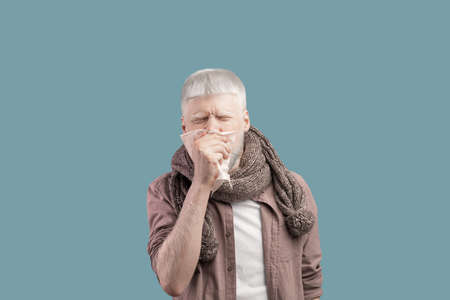 Seasonal flu. Sick albino guy blowing his nose into paper napkin, standing over studio backgroundの写真素材