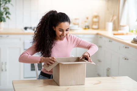Excited happy young woman unboxing cardboard parcel In kitchenの写真素材