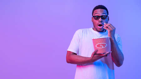 Young African Guy In 3D Glasses Eating Popcorn While Watching Scary Movieの写真素材