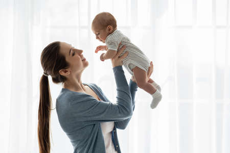 Happy young mom lifting her adorable little newborn baby in airの写真素材
