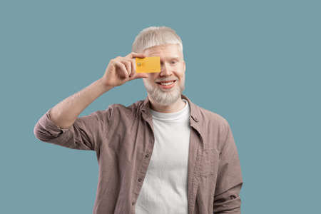 Happy albino man holding credit card in front of his eye on turquoise studio backgroundの写真素材