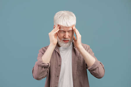 Exhausted young albino man suffering from headache, rubbing temples with closed eyes on blue studio backgroundの写真素材