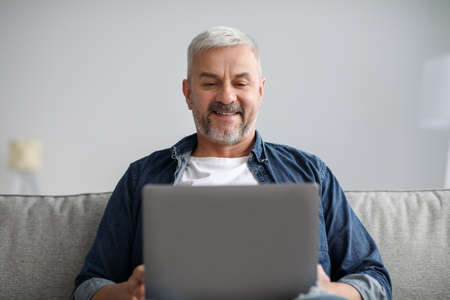 Closeup of relaxed senior man using laptop at home