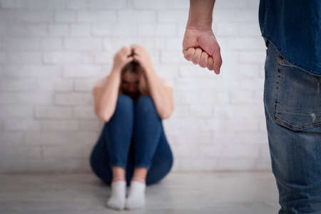 Domestic violence, tyranny and beating. Terrified woman covers her head with hands and sits on floorの写真素材