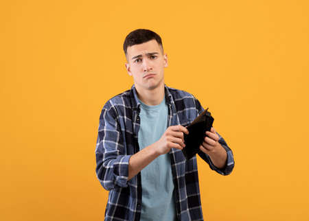 Bankruptcy concept. Upset young man showing empty wallet, suffering from loss of money on orange...