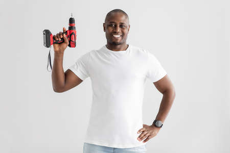 Instruments for renovation. Happy african american man holding electric drill, isolated on white...