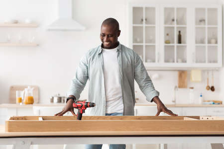Happy african american man ready to installing wooden desk after home relocation, looking at new tableの写真素材