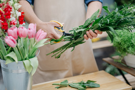 Man entrepreneur in apron working at own flower shop making bouquet aloneの写真素材