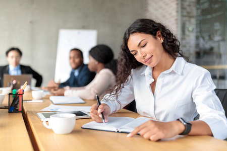 Businesswoman Writing In Notebook Sitting At Conference Meeting In Officeの写真素材