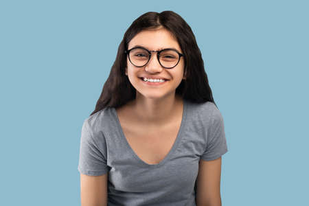 Cute Indian teenage girl in casual outfit and glasses looking at camera on blue studio backgroundの写真素材
