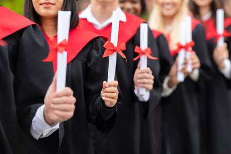 Unrecognizable multiracial group of graduators showing diploma scrolls, closeupの写真素材