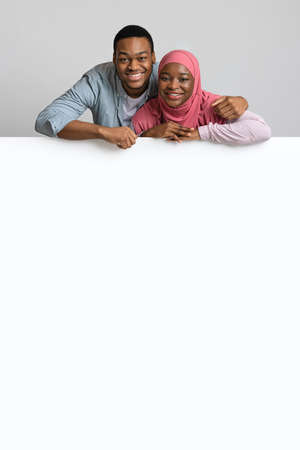 Cute african american couple leaning on white empty boardの写真素材