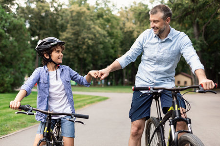 Man giving fist bump to son riding bicycles at parkの写真素材