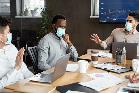 Black employee in protective medical mask coughing near scared colleaguesの写真素材