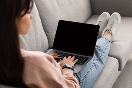 Woman using laptop with blank mockup screen, typing on keyboardの写真素材