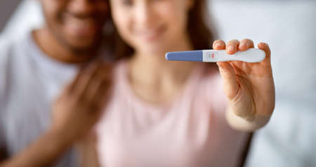 We gonna be parents. Happy multiracial couple in love showing positive pregnancy test on camera, selective focusの写真素材