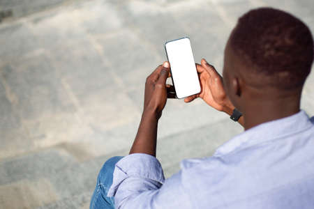 African American man holding smartphone with blank screen on stone staits outside, mockup for mobile app designの写真素材