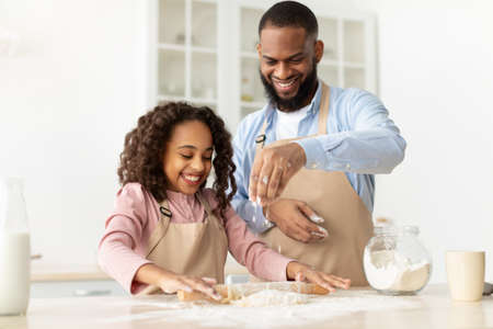 Happy black man and his child daughter kneading doughの写真素材