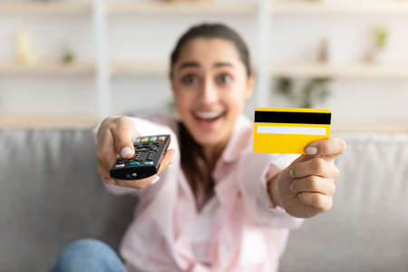 Excited woman holding remote control and debit credit cardの写真素材