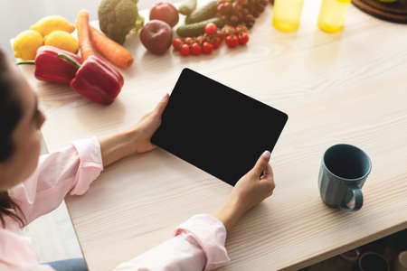 Woman using tablet with empty screen for mockup in kitchenの写真素材