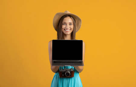 Happy woman traveller holding laptop with blank screen