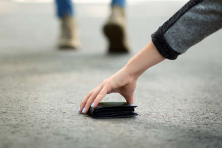 Close up view of young woman picking up lost wallet on city street, empty spaceの写真素材