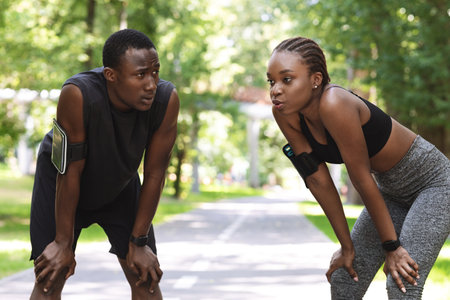Tired African Couple Taking Breath After Hard Workout Outdoors, Resting Togetherの写真素材