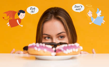 Hungry young woman peeking from under table, looking at donuts, tempted by devil, supported by...