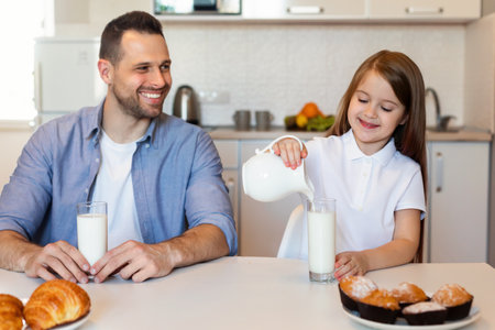Father Looking At Daughter Pouring Milk In Glass In Kitchenの写真素材