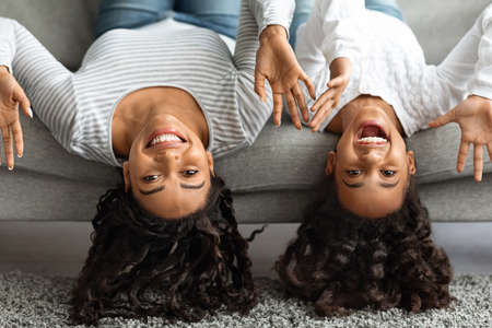 Funny mother and daughter laying on couch upside down