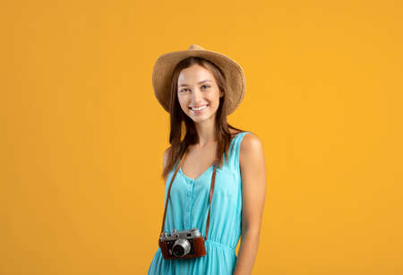 Happy woman tourist with camera posing on yellow