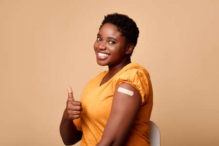 Smiling Black Woman Showing Vaccinated Arm And Thumbs-Up, Beige Backgroundの写真素材
